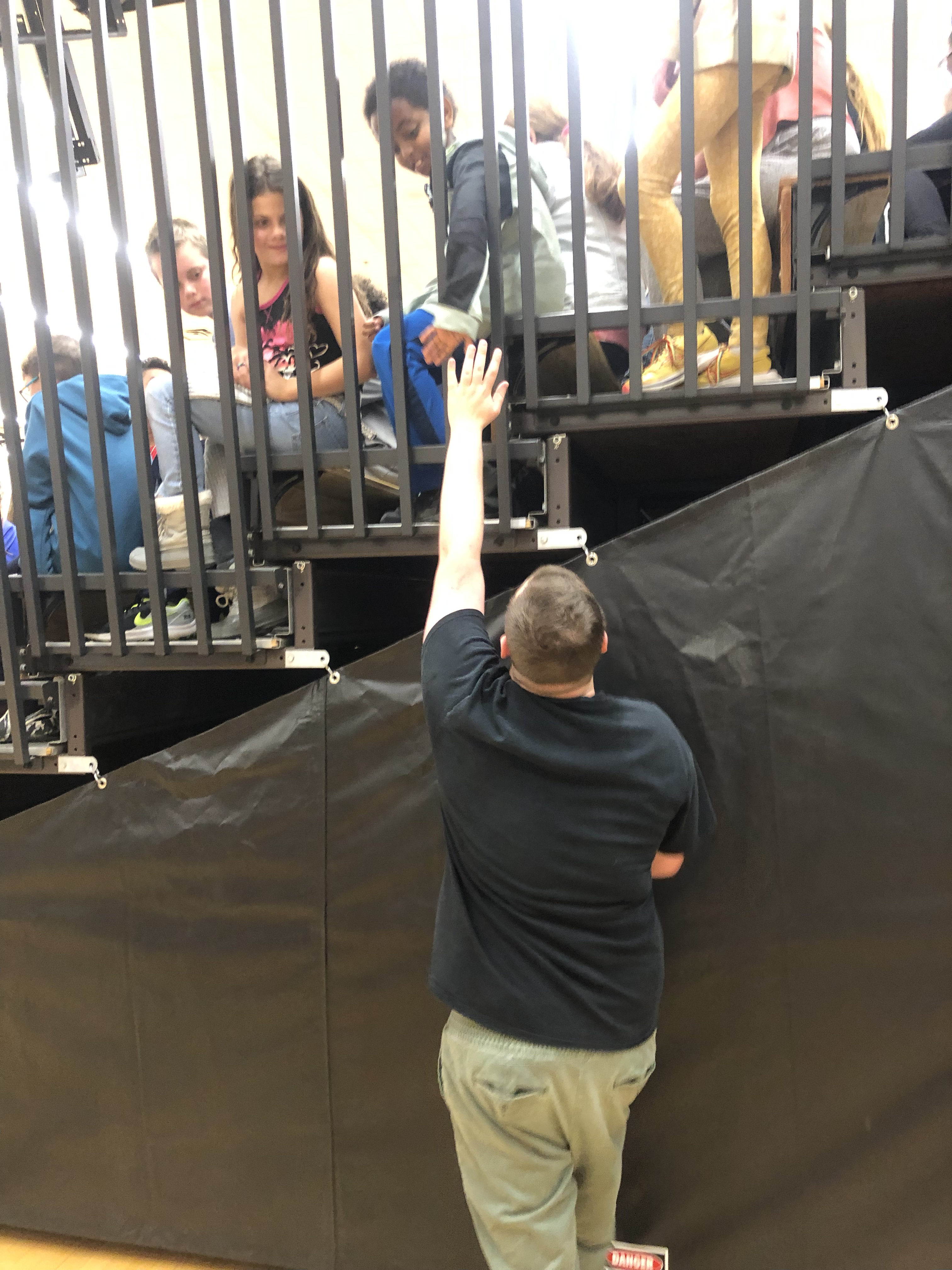Sam reaches up into the bleachers to touch the hand of a fan. The fan smiles broadly.