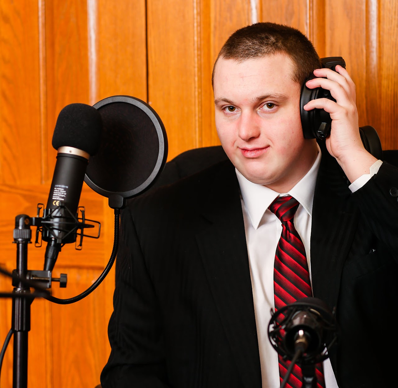 A photo of Sam Mitchell. He's wearing a suit and has a recording microphone and headset.